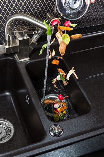 Sink faucet running water down the drain with food scraps.