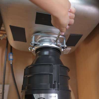 Hand grasping tool and repairing a garbage disposal under a sink.