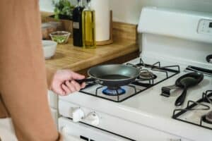 person holds a pan on a gas stove